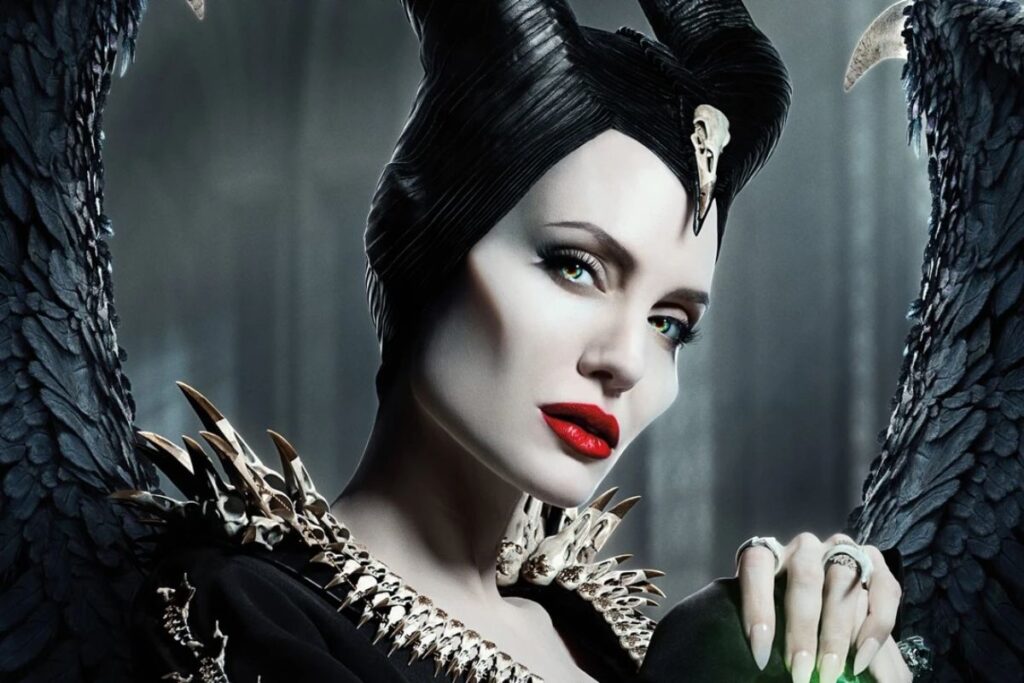Primo piano di Angelina Jolie nei panni di Malefica, con corna nere, occhi verdi, labbra rosse e grandi ali piumate scure sullo sfondo.
